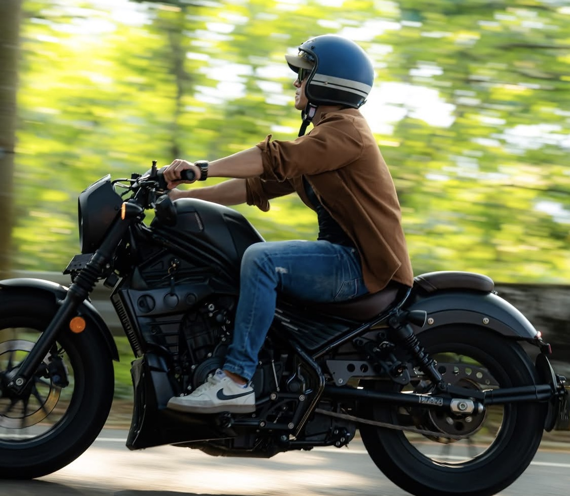 A person riding a black motorcycle while wearing a blue helmet, surrounded by a blurred green background indicating motion.